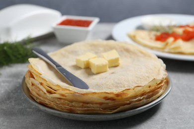 Photo of Stack of tasty crepes with butter on grey textured table, closeup