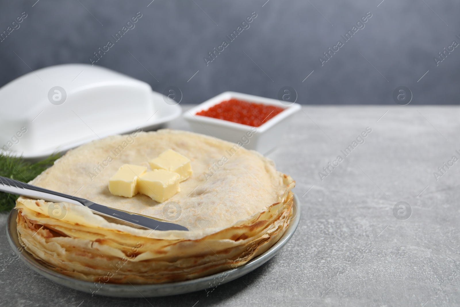 Photo of Stack of tasty crepes with butter on grey textured table, closeup. Space for text