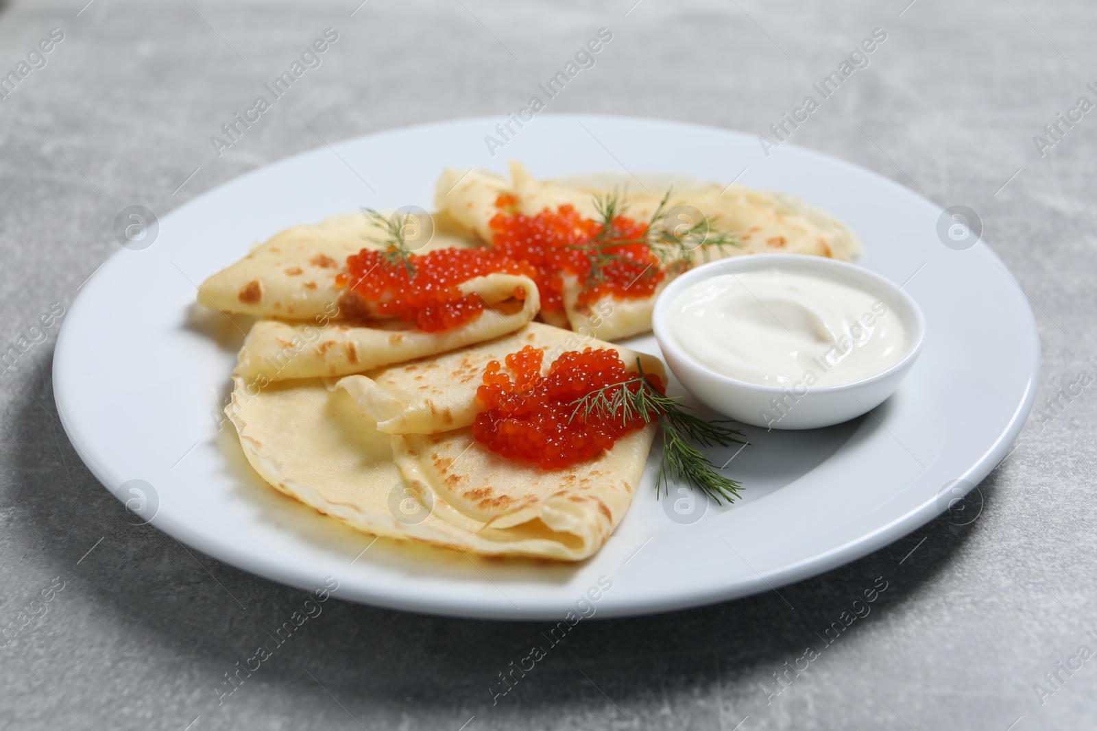 Photo of Tasty crepes with red caviar, dill and sauce on grey textured table, closeup