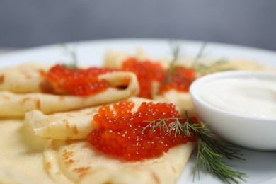 Photo of Tasty crepes with red caviar, dill and sauce on plate, closeup