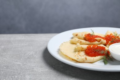 Photo of Tasty crepes with red caviar, dill and sauce on grey textured table, closeup. Space for text