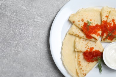 Photo of Tasty crepes with red caviar, dill and sauce on grey textured table, top view. Space for text