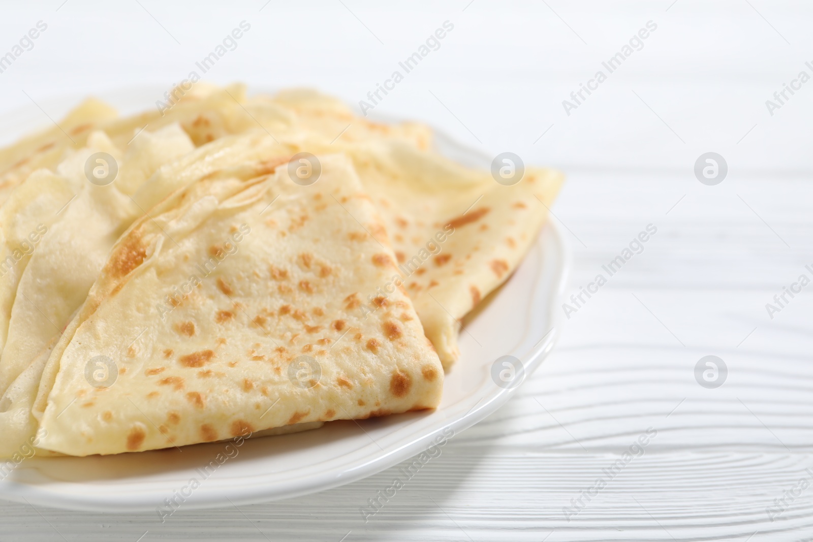 Photo of Tasty crepes on white wooden table, closeup. Space for text