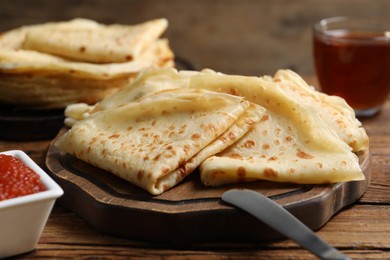 Photo of Tasty crepes and red caviar on wooden table, closeup