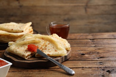 Tasty crepes and red caviar on wooden table, closeup. Space for text