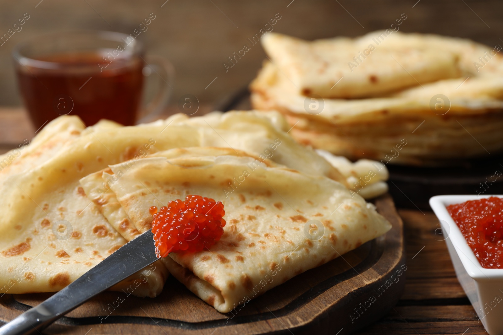 Photo of Tasty crepes and red caviar on wooden table, closeup