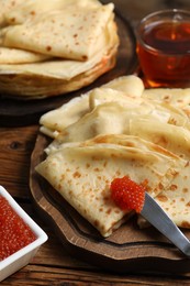 Photo of Tasty crepes and red caviar on wooden table, closeup