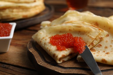 Photo of Tasty crepes and red caviar on wooden table, closeup