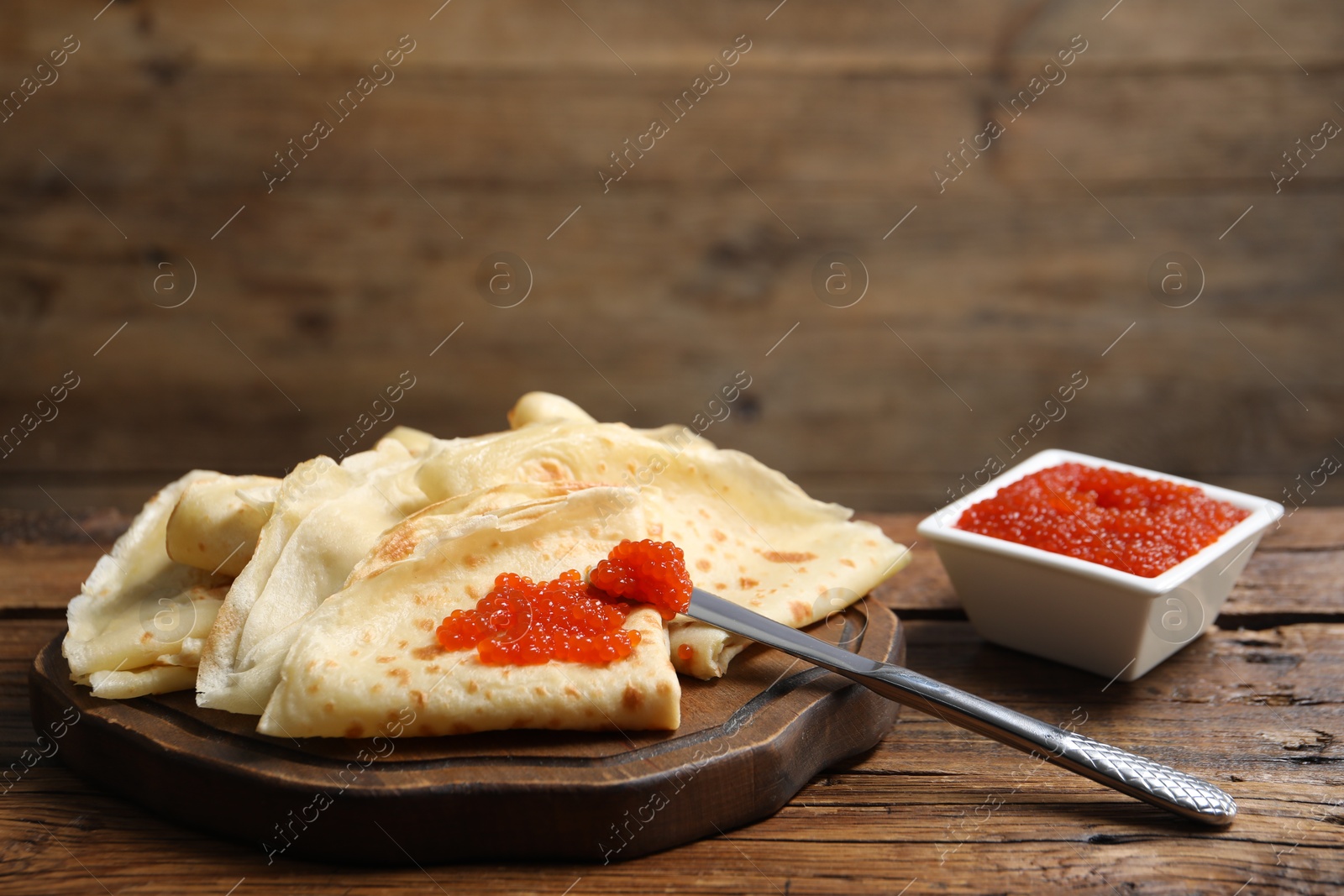 Photo of Tasty crepes and red caviar on wooden table, closeup