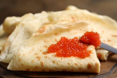 Photo of Tasty crepes and red caviar on wooden board, closeup