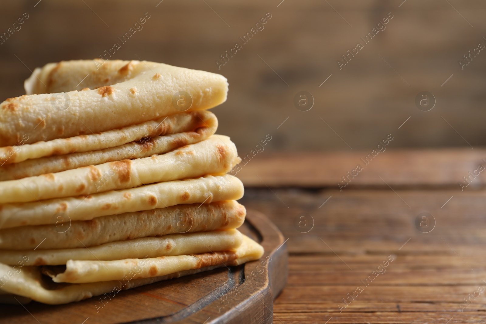 Photo of Stack of tasty crepes on wooden table, closeup. Space for text