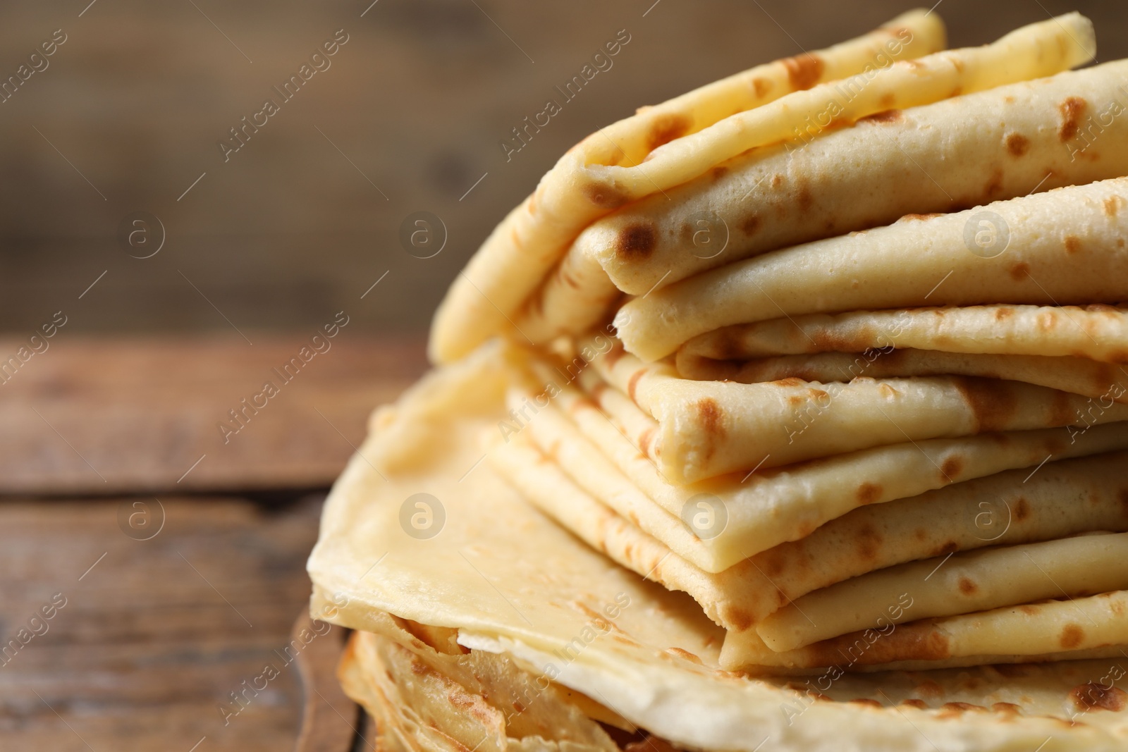 Photo of Stack of tasty crepes on wooden table, closeup. Space for text