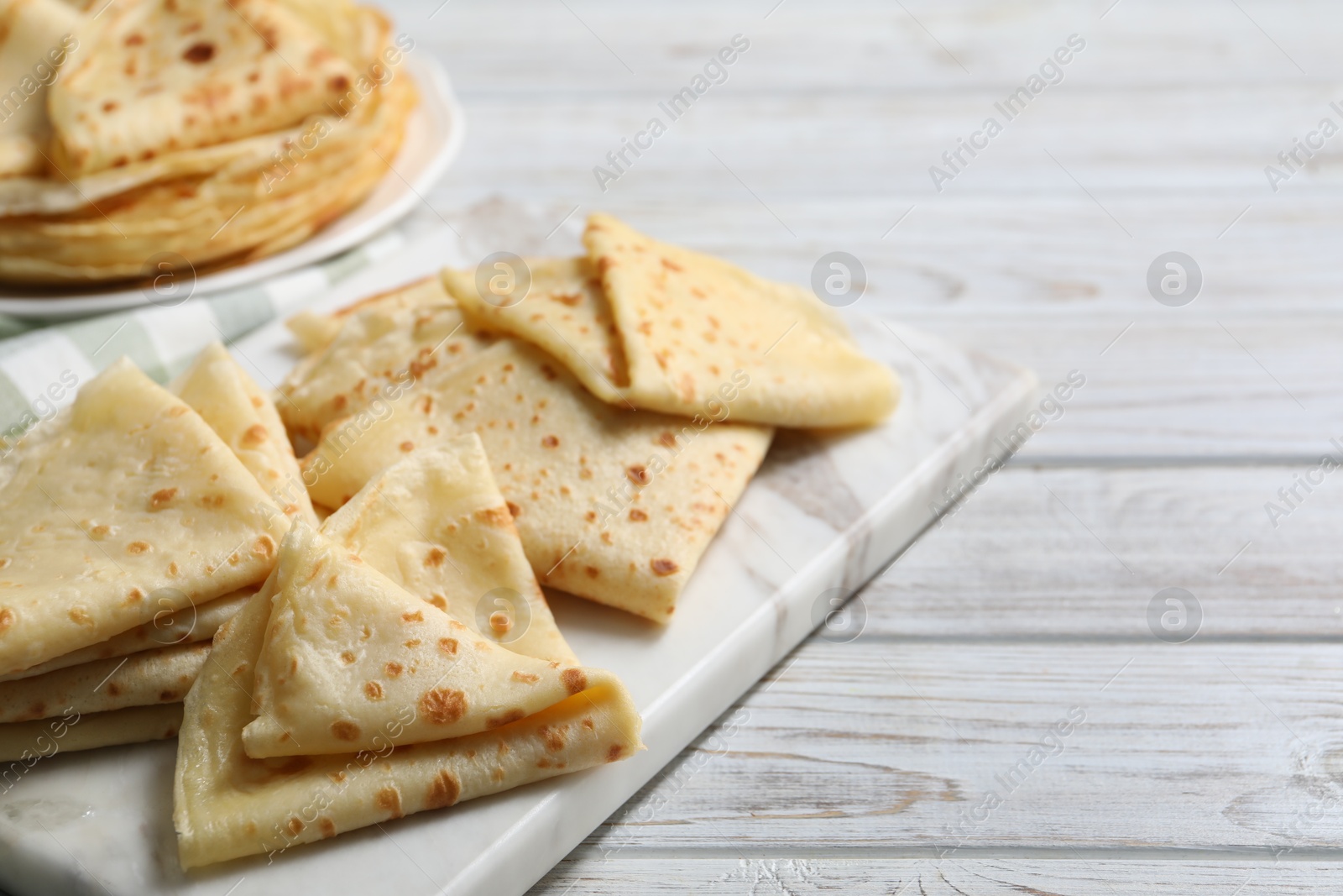 Photo of Many tasty crepes on white wooden table, closeup. Space for text