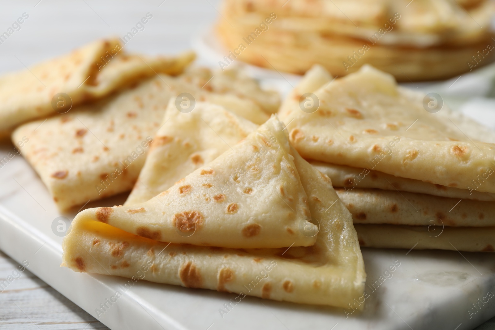 Photo of Many tasty crepes on white wooden table, closeup