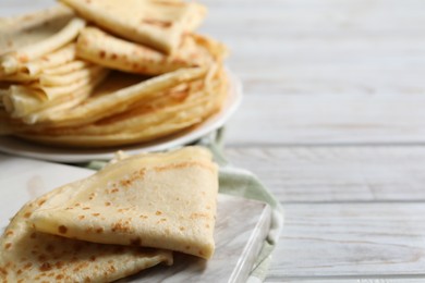 Photo of Many tasty crepes on white wooden table, closeup. Space for text