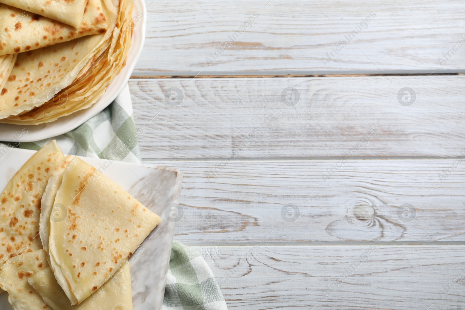 Photo of Many tasty crepes on white wooden table, top view. Space for text