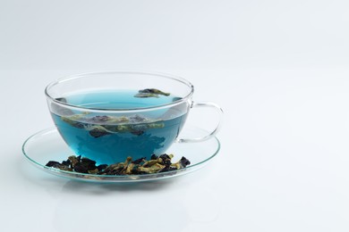 Photo of Fresh butterfly pea flower tea in cup and dry petals on white table, closeup. Space for text