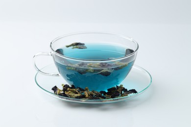 Photo of Fresh butterfly pea flower tea in cup and dry petals on white table, closeup