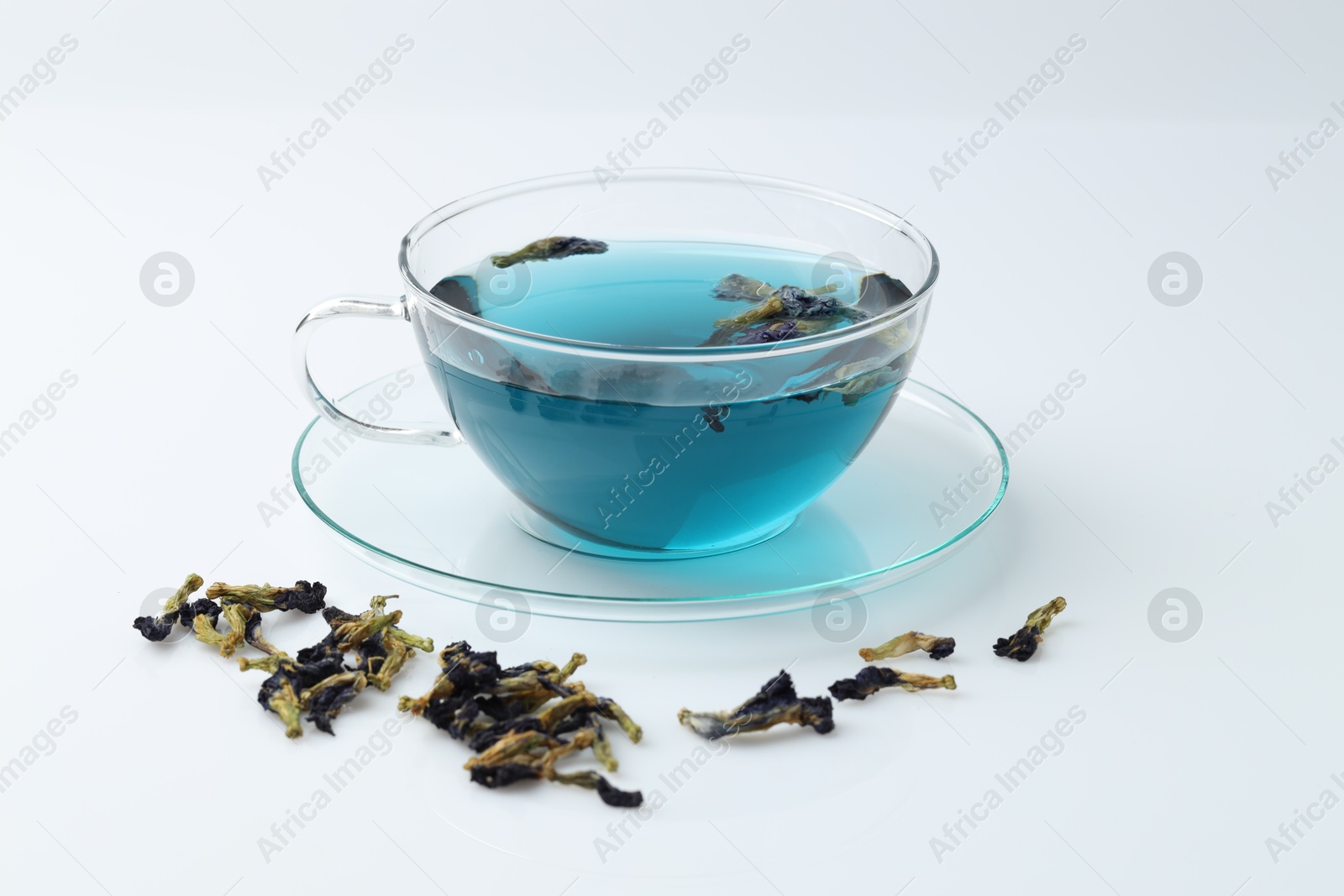 Photo of Fresh butterfly pea flower tea in cup and dry petals on white table, closeup