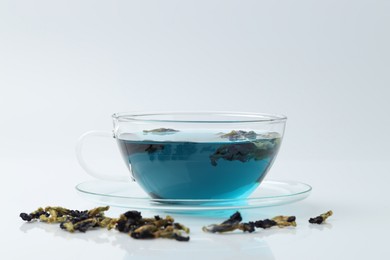 Photo of Fresh butterfly pea flower tea in cup and dry petals on white table, closeup