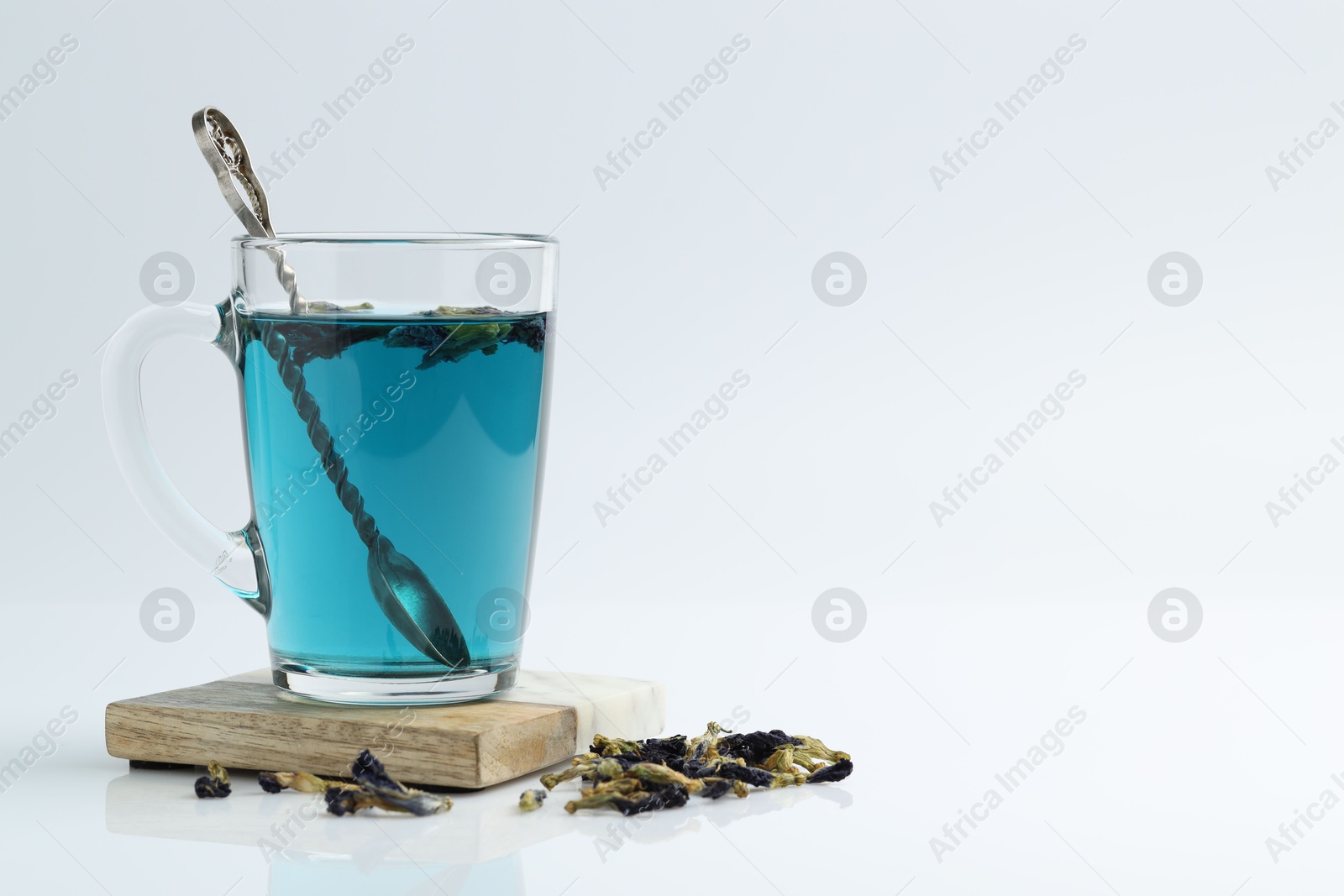 Photo of Fresh butterfly pea flower tea in cup and dry petals on white table, closeup. Space for text