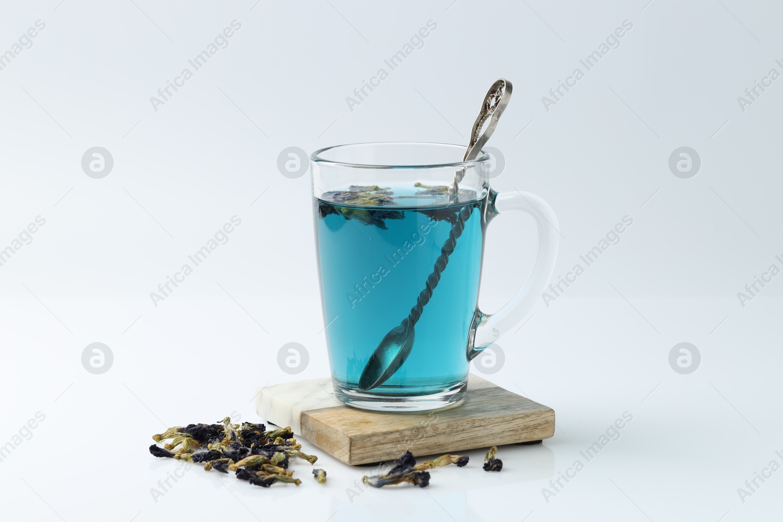 Photo of Fresh butterfly pea flower tea in cup and dry petals on white table, closeup