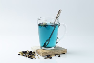 Photo of Fresh butterfly pea flower tea in cup and dry petals on white table, closeup