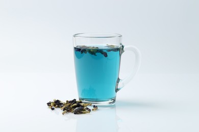 Photo of Fresh butterfly pea flower tea in cup and dry petals on white table, closeup