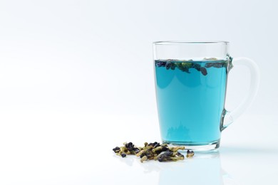 Photo of Fresh butterfly pea flower tea in cup and dry petals on white table, closeup. Space for text