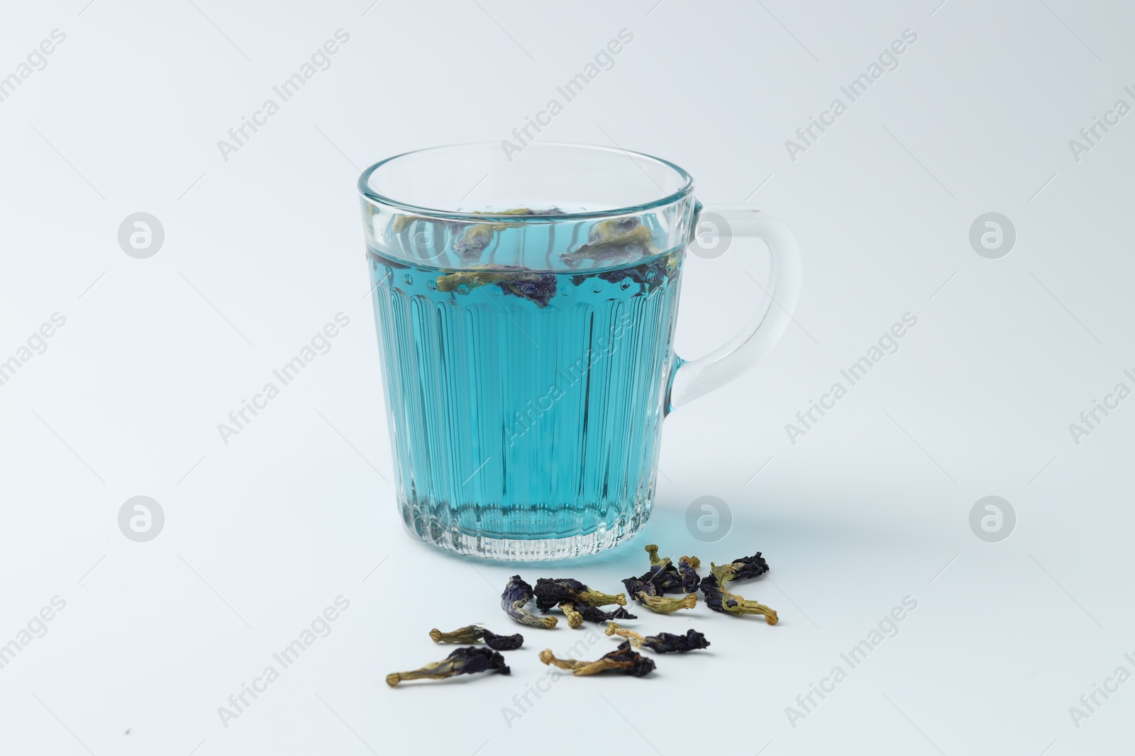 Photo of Fresh butterfly pea flower tea in cup and dry petals on white table, closeup