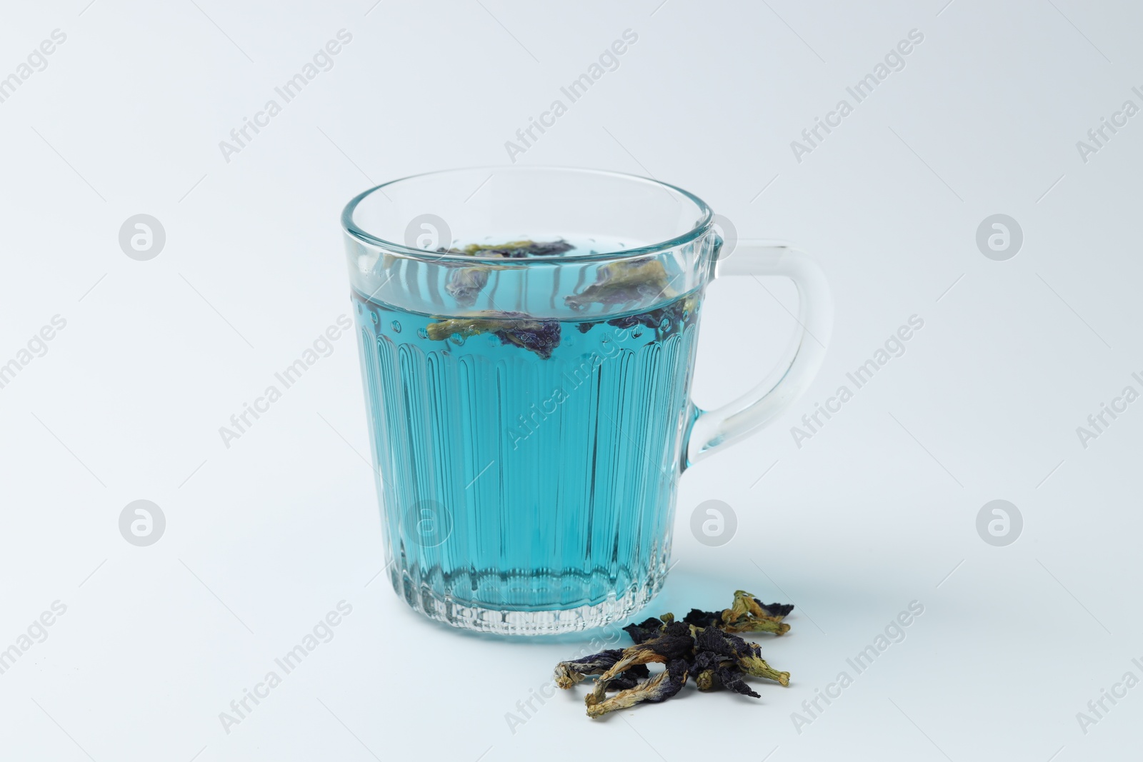 Photo of Fresh butterfly pea flower tea in cup and dry petals on white table, closeup