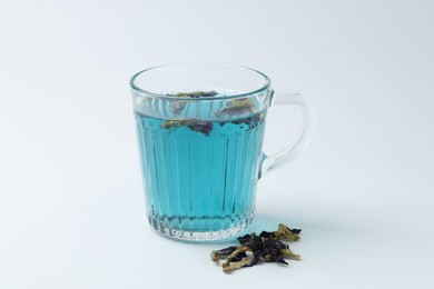 Photo of Fresh butterfly pea flower tea in cup and dry petals on white table, closeup