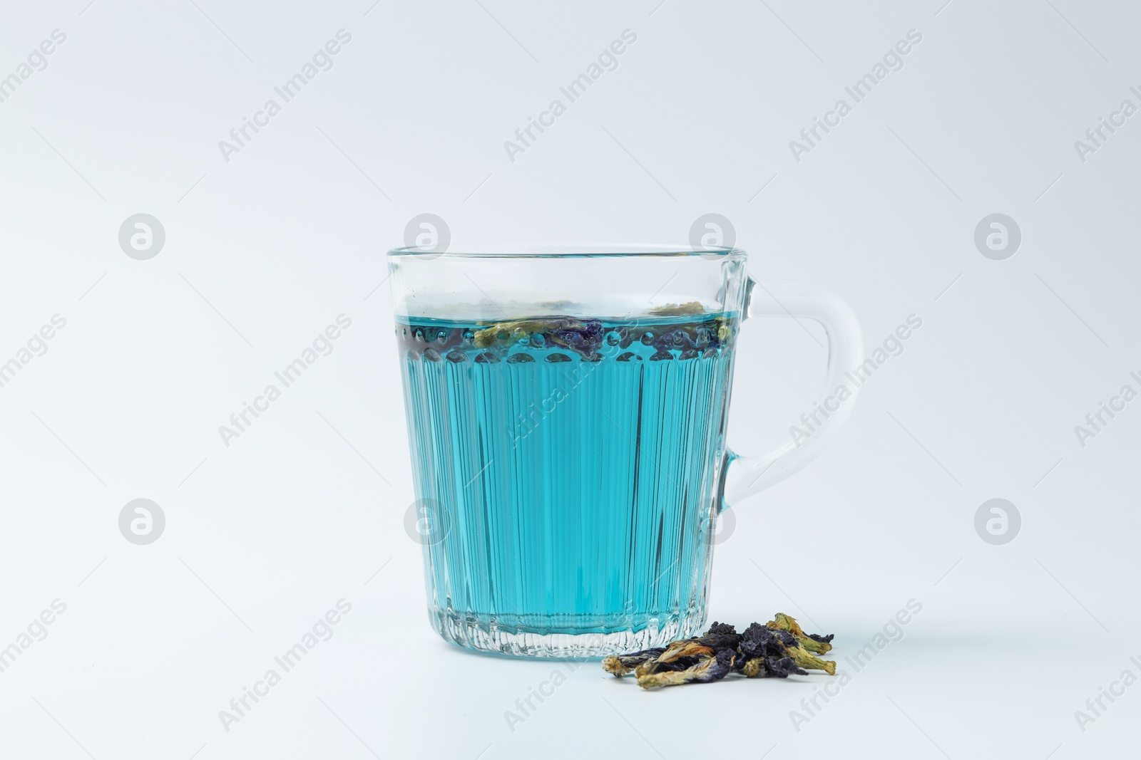 Photo of Fresh butterfly pea flower tea in cup and dry petals on white table, closeup