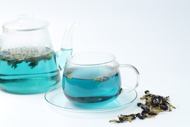 Photo of Fresh butterfly pea flower tea in cup, kettle and dry petals on white table, closeup