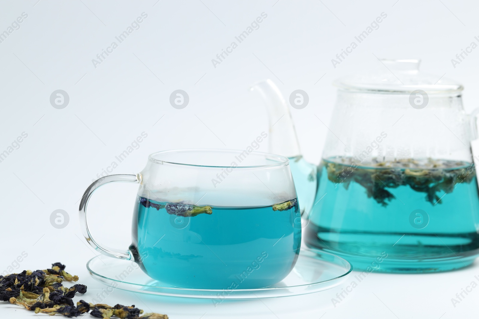 Photo of Fresh butterfly pea flower tea in cup, kettle and dry petals on white table, closeup