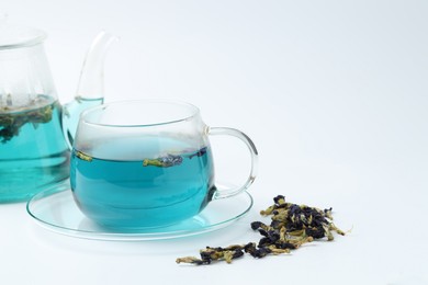 Photo of Fresh butterfly pea flower tea in cup, teapot and dry petals on white table, closeup. Space for text