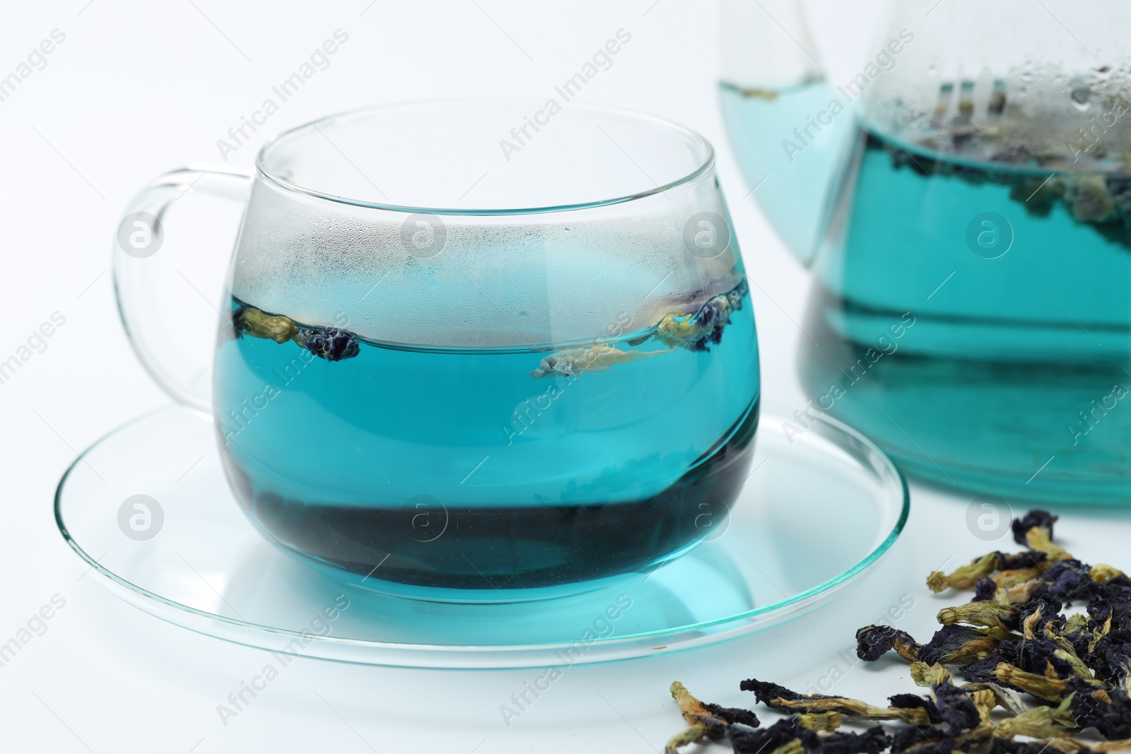 Photo of Fresh butterfly pea flower tea in cup and dry petals on white table, closeup