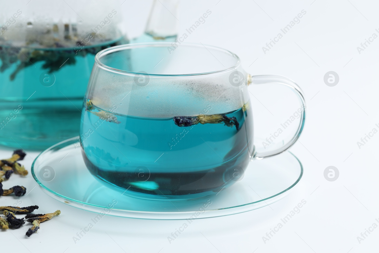 Photo of Fresh butterfly pea flower tea in cup and dry petals on white table, closeup