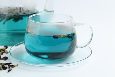 Photo of Fresh butterfly pea flower tea in cup and dry petals on white table, closeup