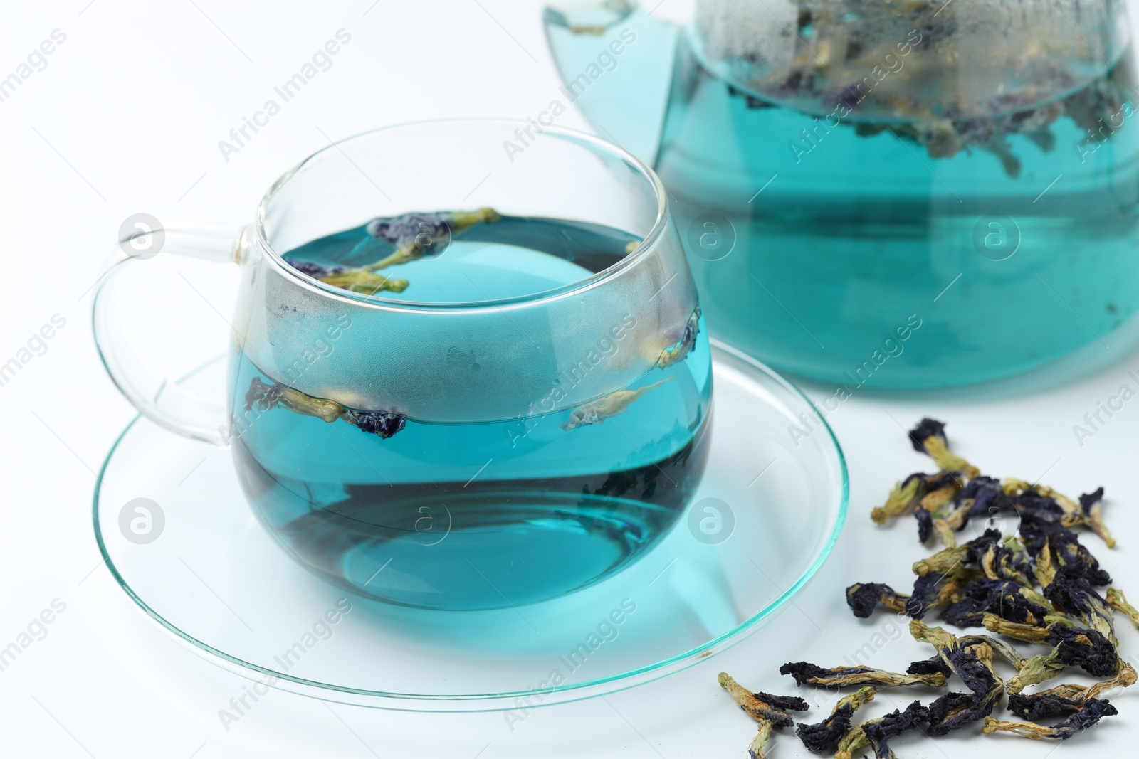 Photo of Fresh butterfly pea flower tea in cup and dry petals on white table, closeup