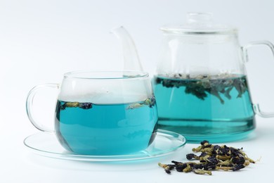 Photo of Fresh butterfly pea flower tea in cup, kettle and dry petals on white table, closeup