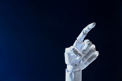 Photo of Artificial intelligence. Robot hand pointing at something on dark blue background, space for text