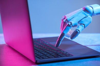 Photo of Artificial intelligence. Robot hand using laptop on table in neon lights, closeup