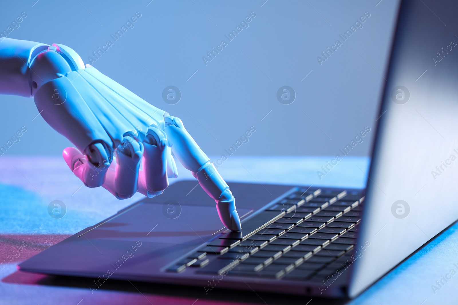 Photo of Artificial intelligence. Robot hand using laptop on table in neon lights, closeup