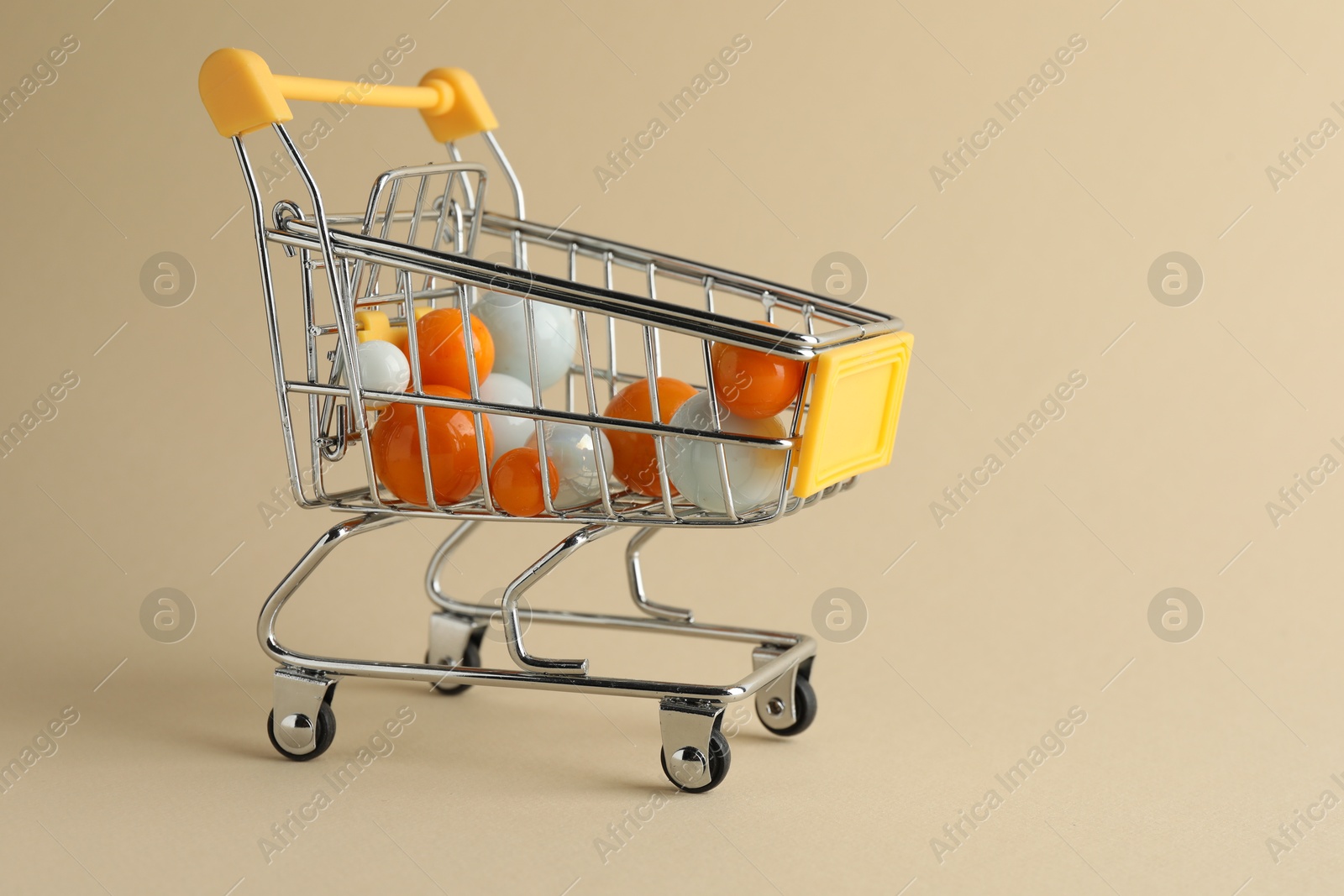 Photo of Small metal shopping cart with colorful balls on beige background, space for text