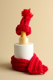 Photo of Bottle of skin care product with red knitted hat and scarf on beige background