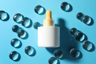 Photo of Bottle of skin care product and transparent decorative stones on light blue background, flat lay