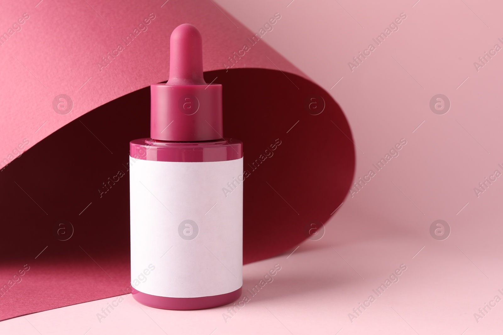 Photo of Bottle of skin care product on pink background, space for text