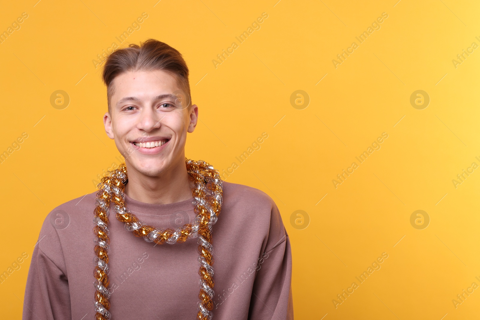 Photo of Happy young man with tinsel on orange background, space for text