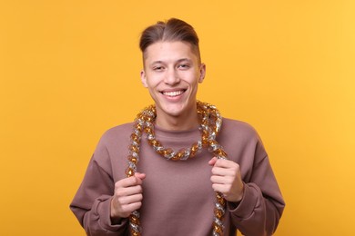 Photo of Happy young man with tinsel on orange background